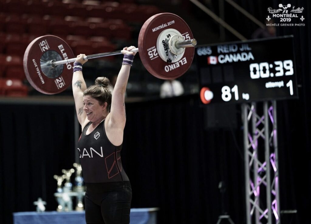 Masters weightlifter Jill Reid locking out 81 kilograms overhead in competition at Montreal 2019, wearing a Canada singlet.
