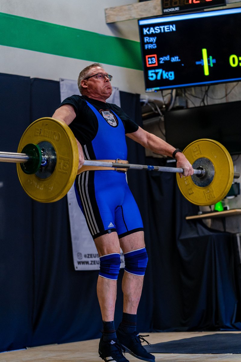 Masters weightlifter Ray Kasten pulling 57 kilograms on his second attempt, the scoreboard behind him showing his name and the weight.