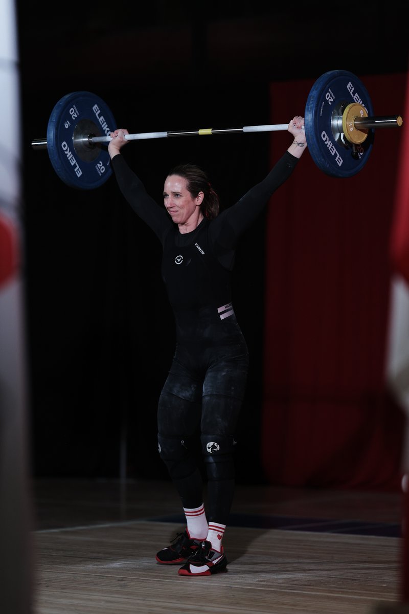 Masters weightlifter Shannon Parrett holding a jerk locked out overhead in competition, arms straight and feet settled on the platform.